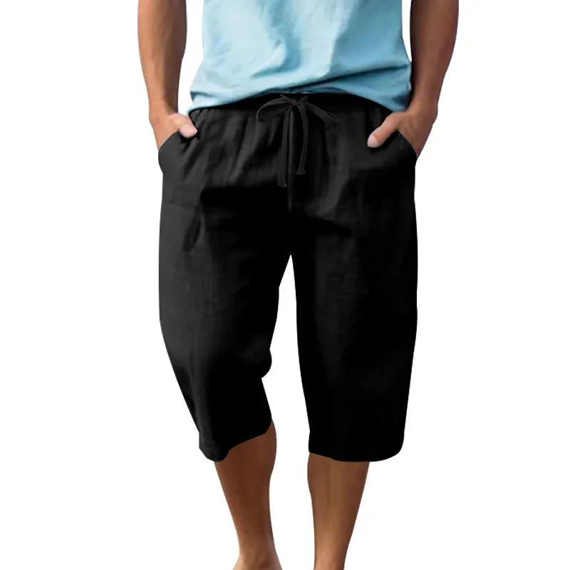 Man wearing loose-fit light khaki linen shorts with a drawstring waist and cropped leg.
