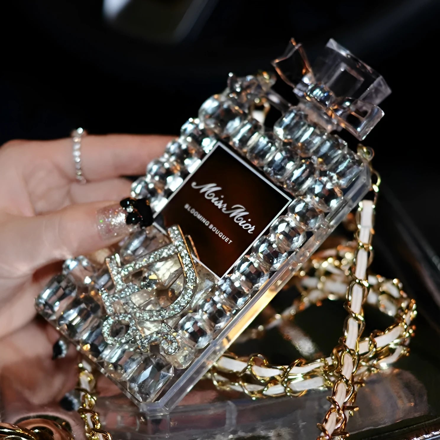 iPhone case with a perfume bottle and bow charm on a metal chain, in black colour with textured TPU shell.