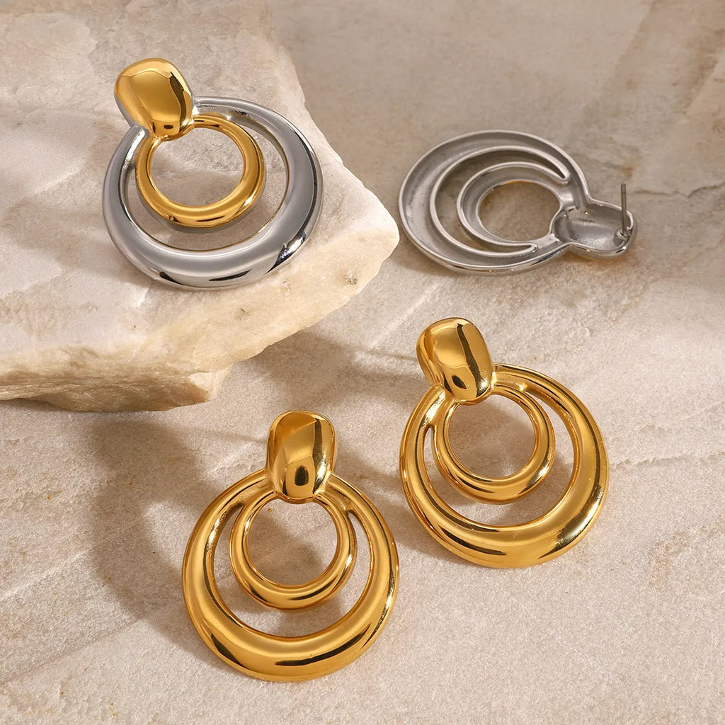 A pair of round, golden, hollow double layer stud earrings made from titanium steel with 18K gold electroplating.