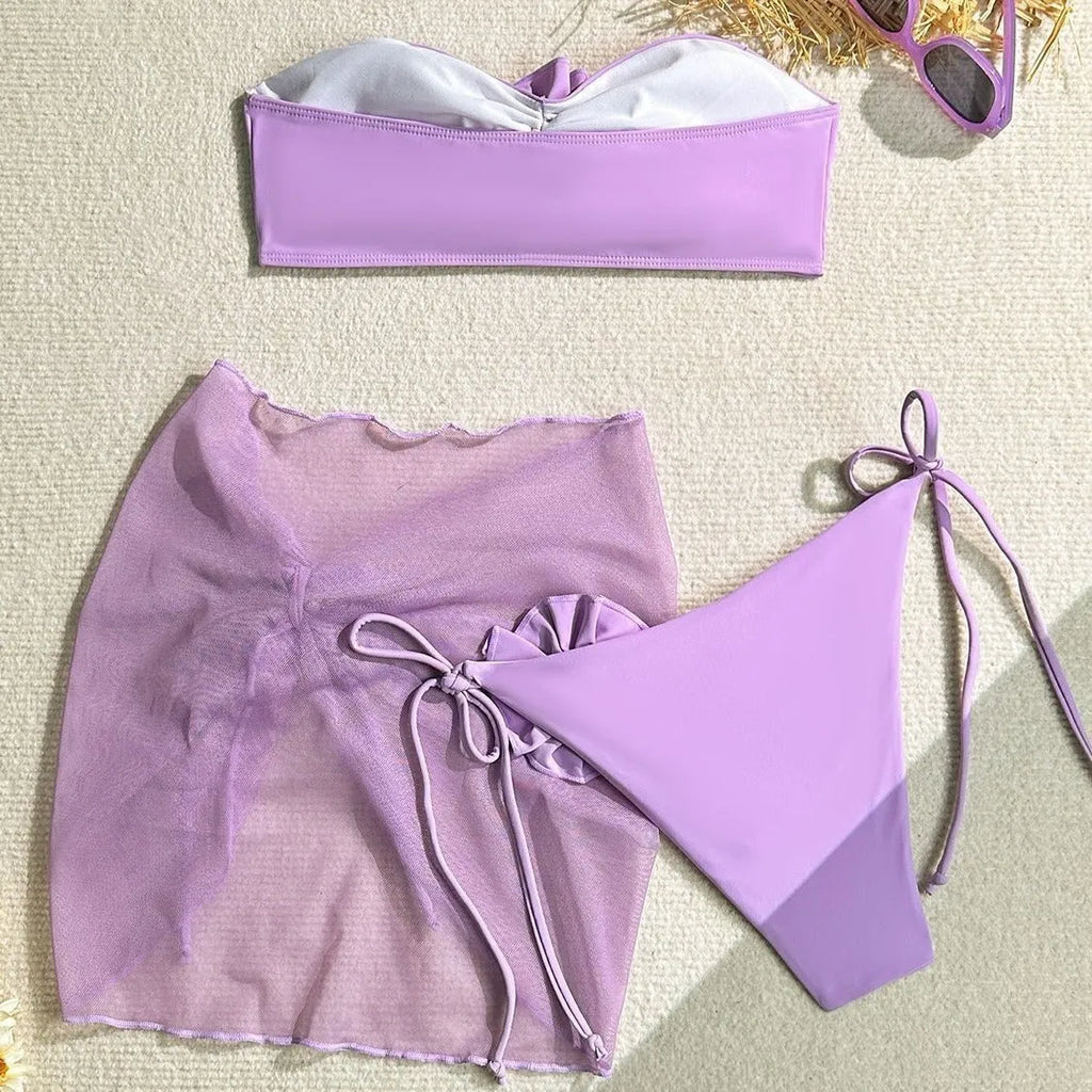 Women's pink tie-front halter swimsuit with 3D flower, high-waisted bottoms, and matching skirt laid flat.