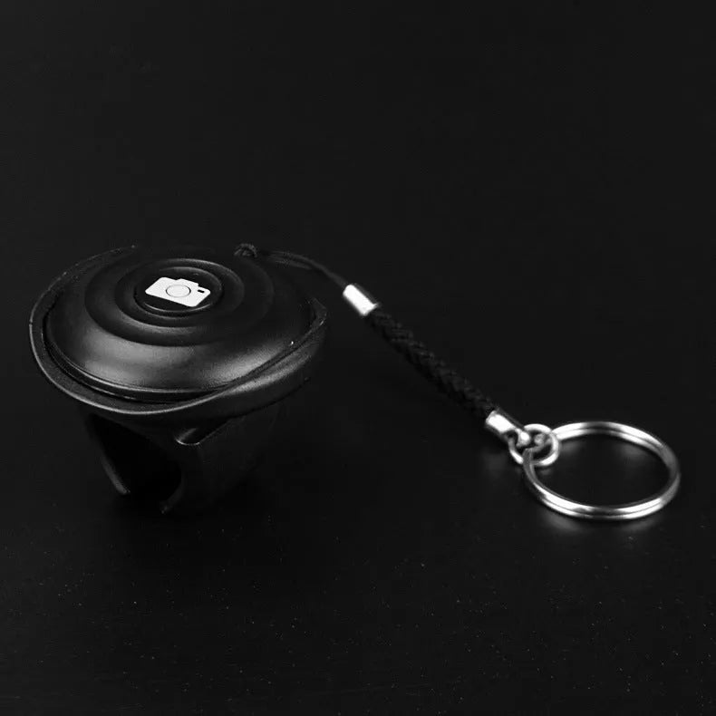 Small black Bluetooth selfie remote on a palm, showcasing its compact size and single button.