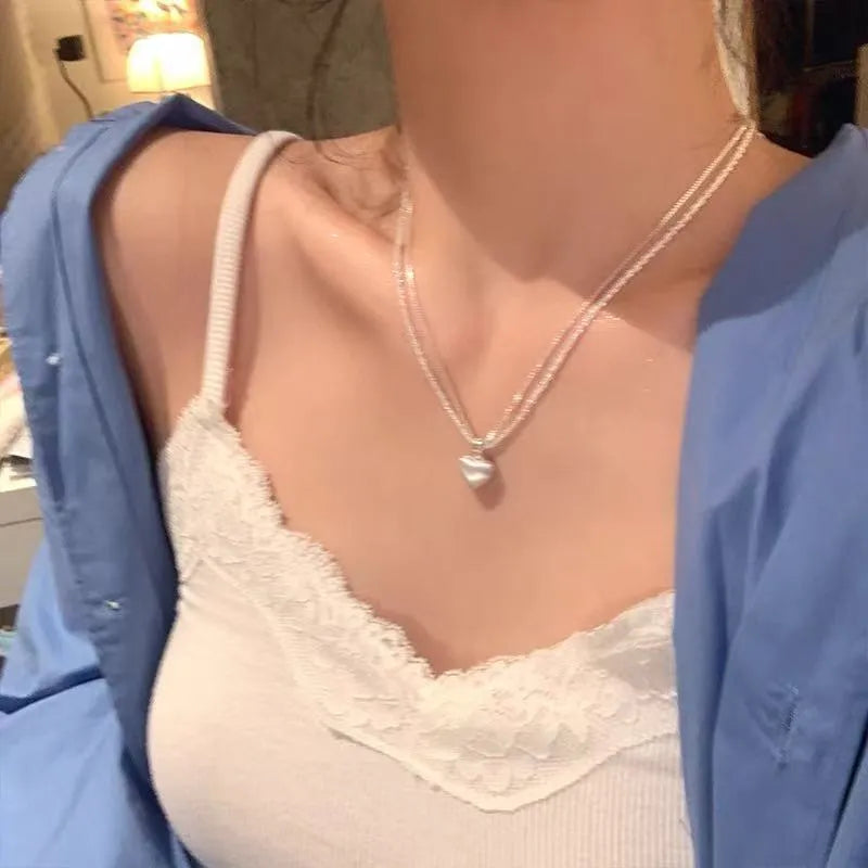 Double-layer brushed silver heart pendant necklace on a model, showing adjustable chain length.