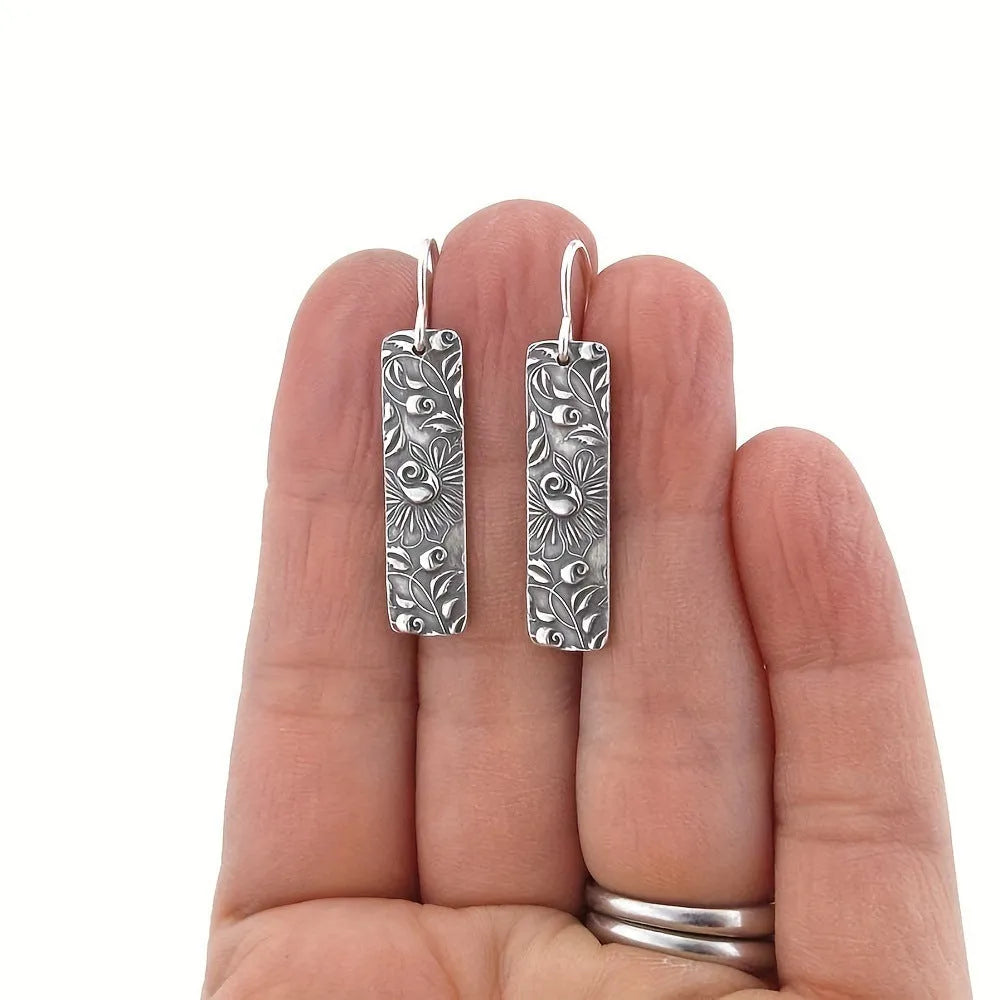 Silver geometric long strip drop earrings with carved vine pattern on a white background.