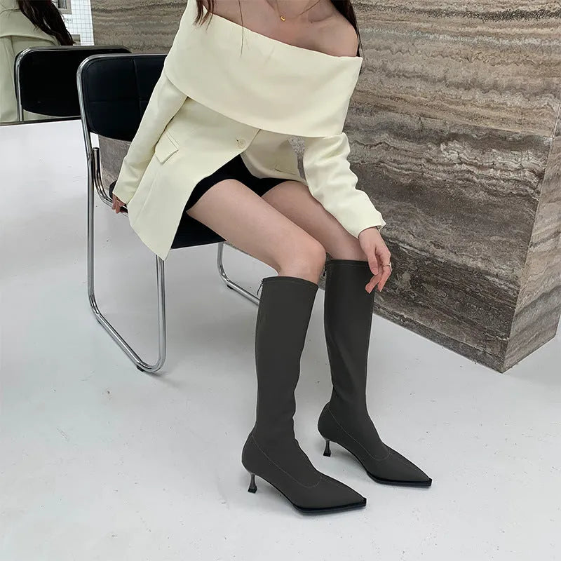 Black pointed-toe below-knee women's boots with a stiletto heel and a visible back zip on a neutral background.
