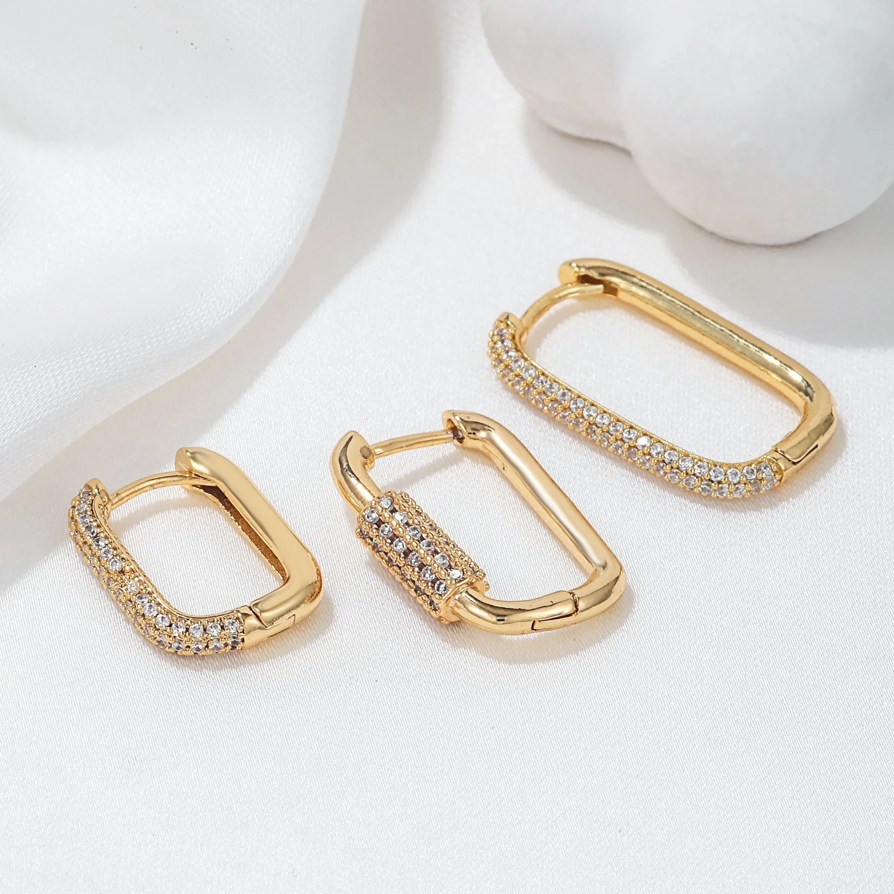 Three geometric copper earrings with inlaid zircon on a square clip, in gold and white finishes.
