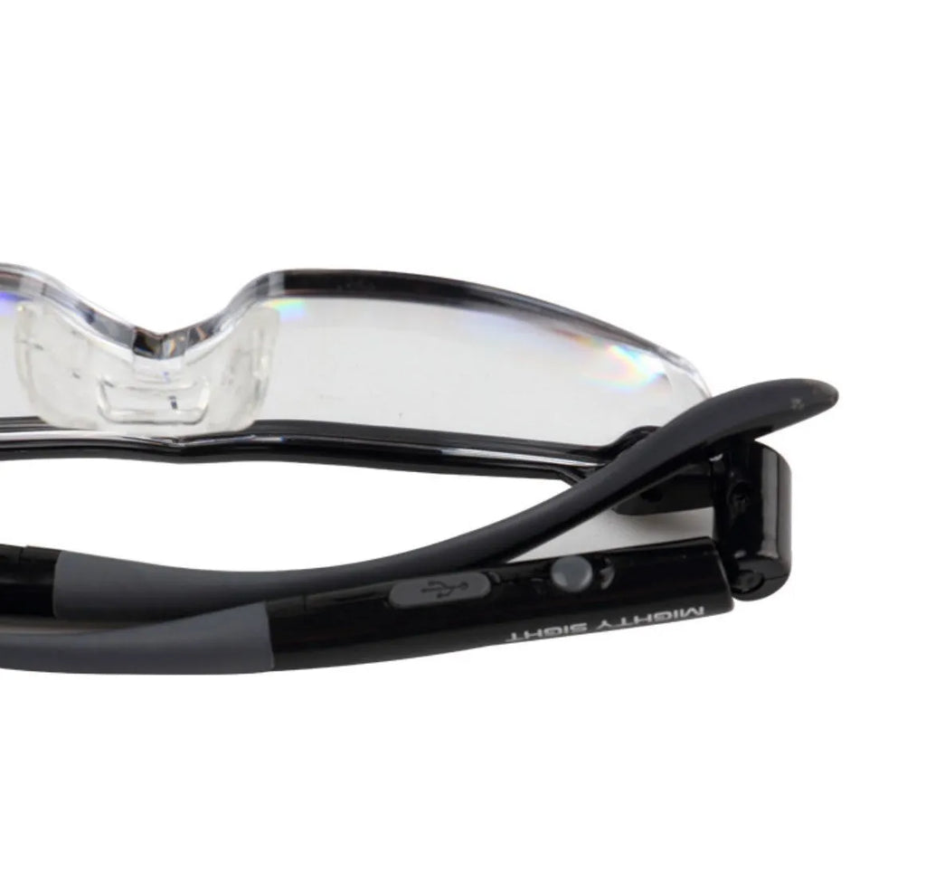Transparent black USB LED light reading glasses on a table, showing the integrated light and frame.