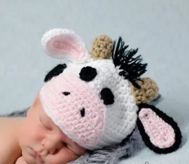 Hand-knitted white baby cow suit with hat and trousers for a newborn.