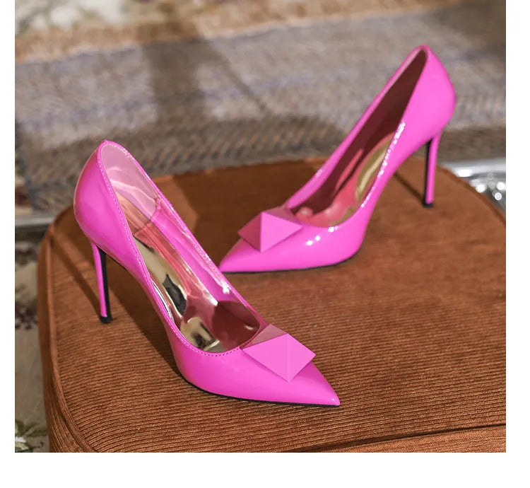 Women's pink patent leather pointed toe stiletto heels with an ankle buckle strap on a white background.
