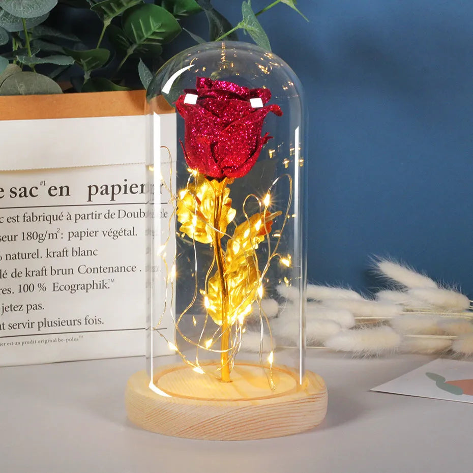 Red eternal rose with warm white LED lights under a glass dome on a table.