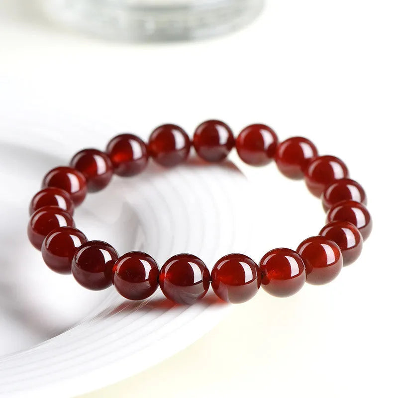 Natural Orange Red Garnet ball bead bracelet with a metal Ruyi charm on a white background.