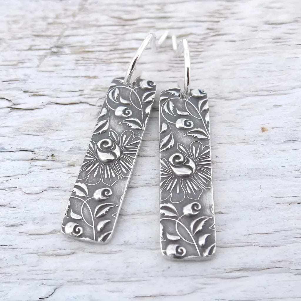 Silver geometric long strip drop earrings with carved vine pattern on a white background.