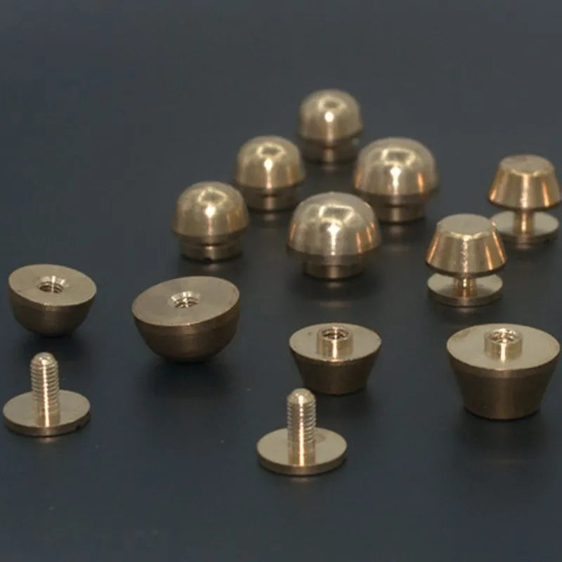 Brass decorative buckle with set of round and bucket-shaped brass foot nails on a surface.