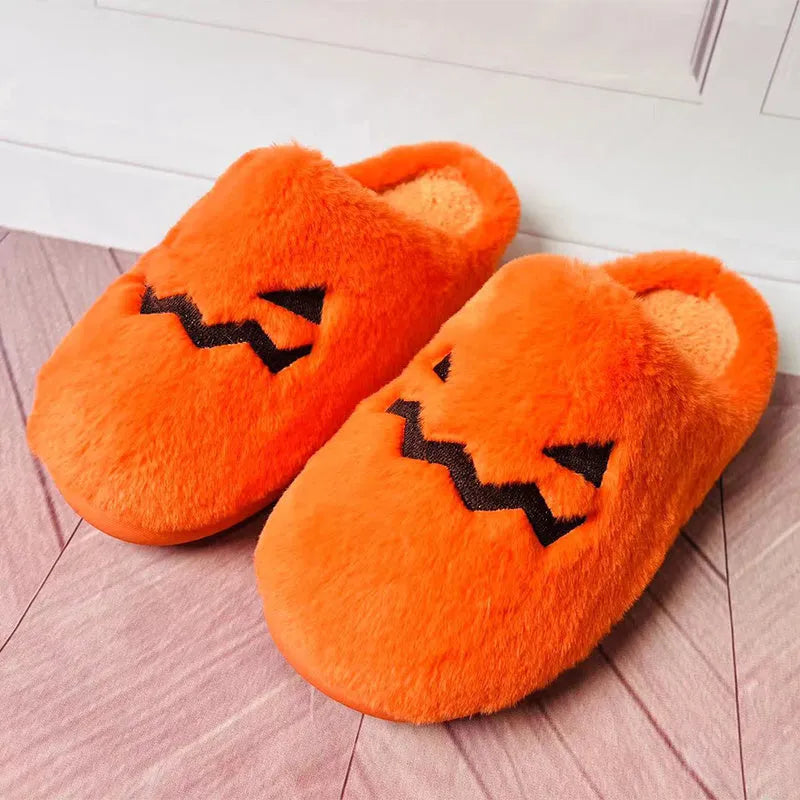 Orange Halloween pumpkin-themed plush indoor slippers with a non-slip sole on a wooden floor.