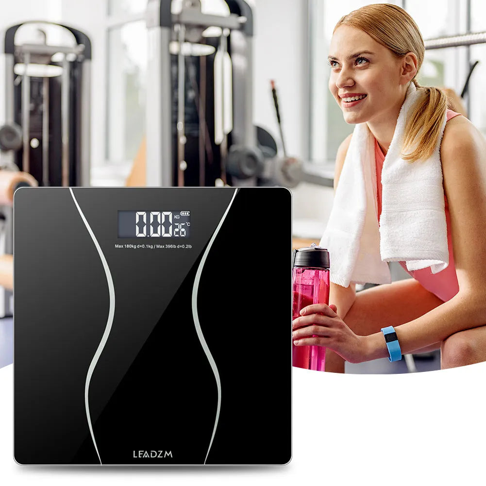 Black digital electronic bathroom scale with tempered glass platform on a bathroom floor.