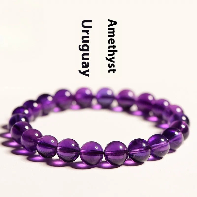 Close-up of a polished natural amethyst bead stretch bracelet on a wrist, showing deep violet colour and elasticated band.