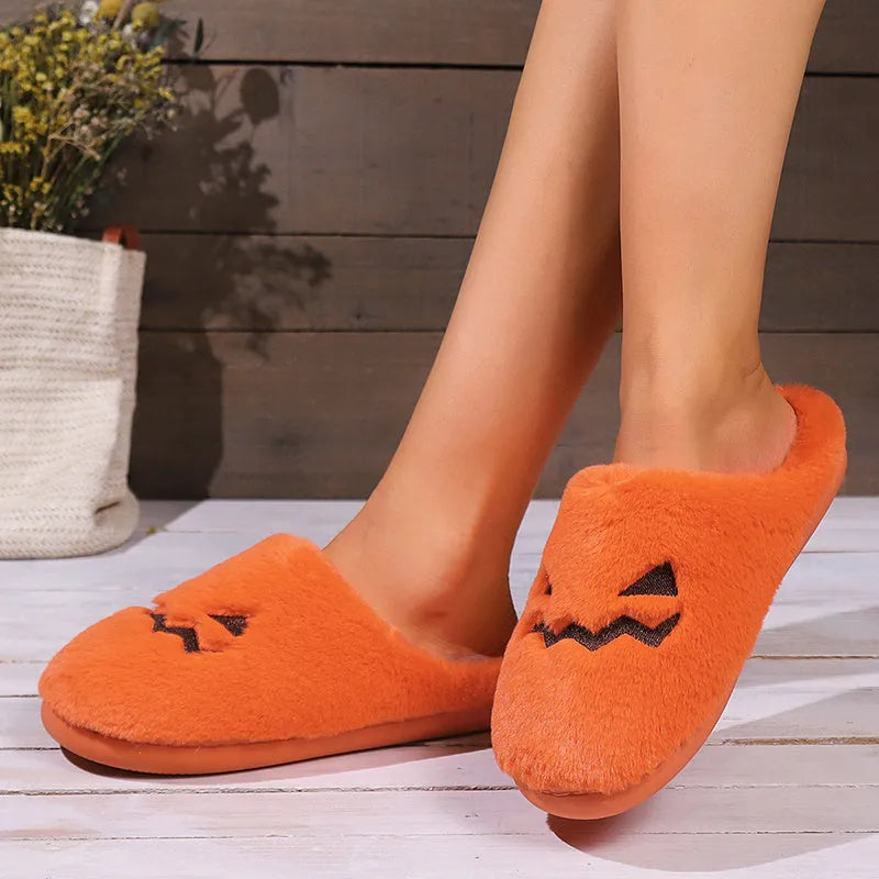 Orange Halloween pumpkin-themed plush indoor slippers with a non-slip sole on a wooden floor.
