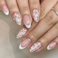 Short almond-shaped plastic false nails with glossy white French tips and pink glitter powder flower design.