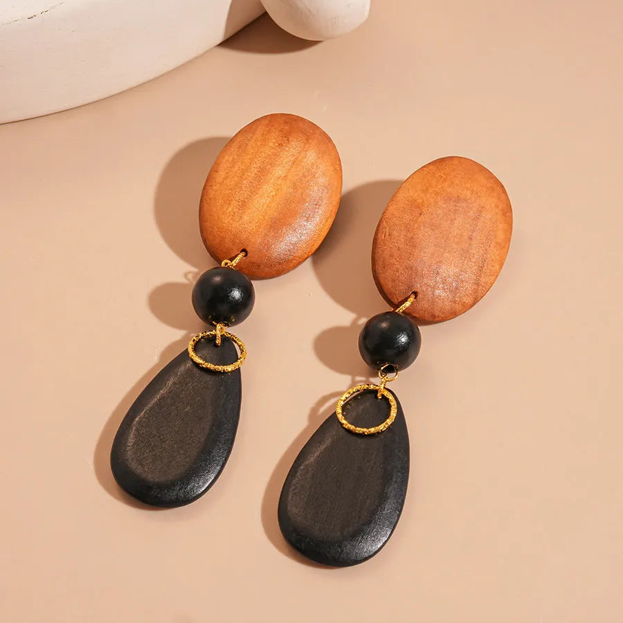 Wooden drop earrings with an ellipse shape in silver, brown, and black colours, showing manual craftsmanship.