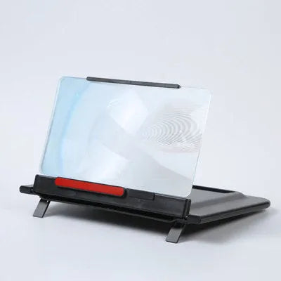 Black 12-inch mobile phone screen amplifier with pull-out stand on a table next to a phone.