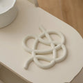 Irregular-shaped ceramic heat proof mat in grey on a wooden table next to a hot pan.