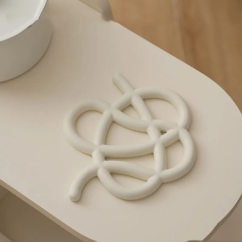 Irregular-shaped ceramic heat proof mat in grey on a wooden table next to a hot pan.