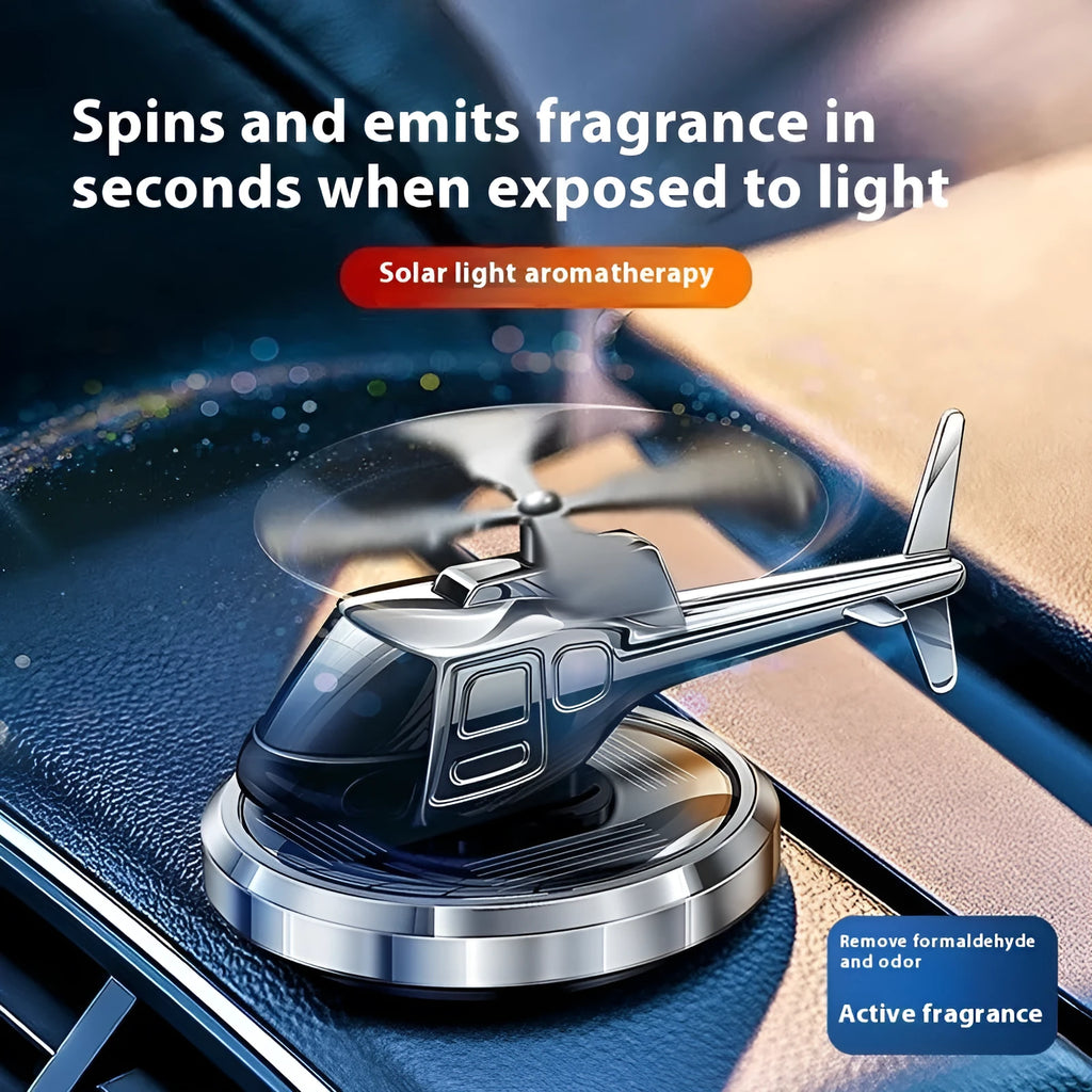 Silver metal solar-powered helicopter car air freshener with spinning blades on a dashboard.