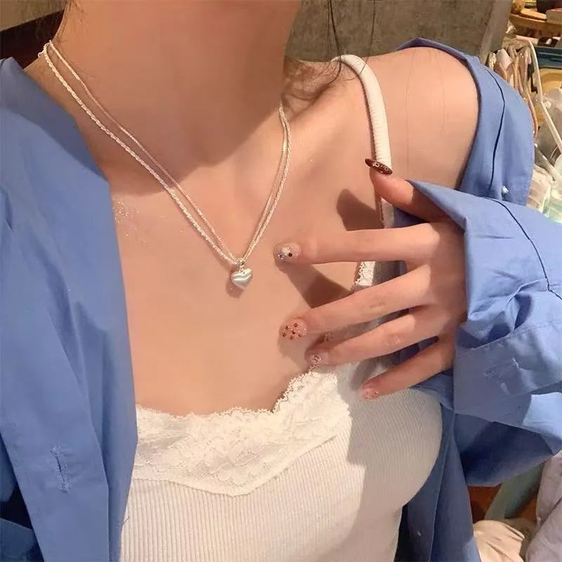 Double-layer brushed silver heart pendant necklace on a model, showing adjustable chain length.