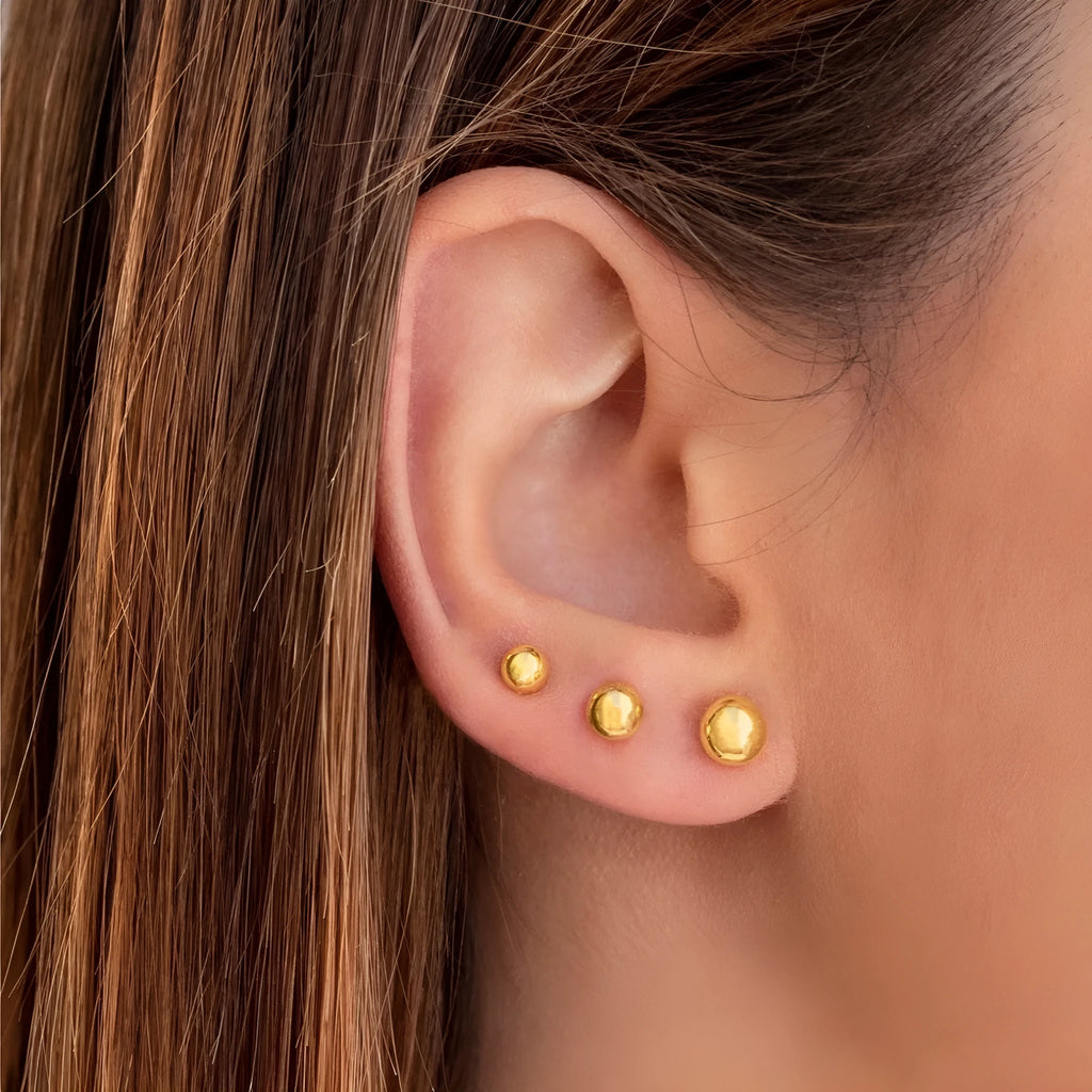 Close-up of a small spherical stainless steel stud earring with a polished electroplated finish on a grey background.