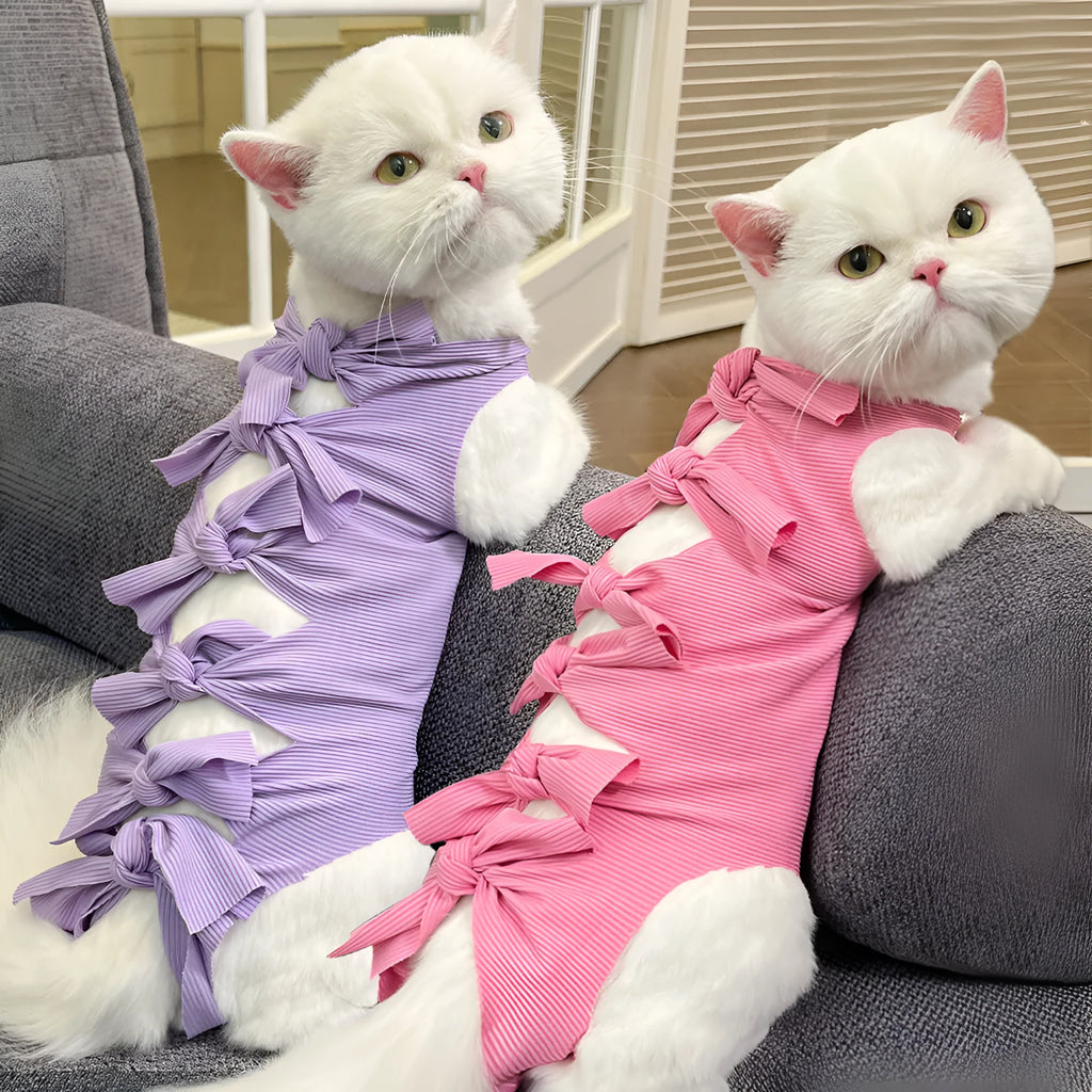 A pink lace-up cat recovery suit on a grey cat, showing the back closure and full-body fit.
