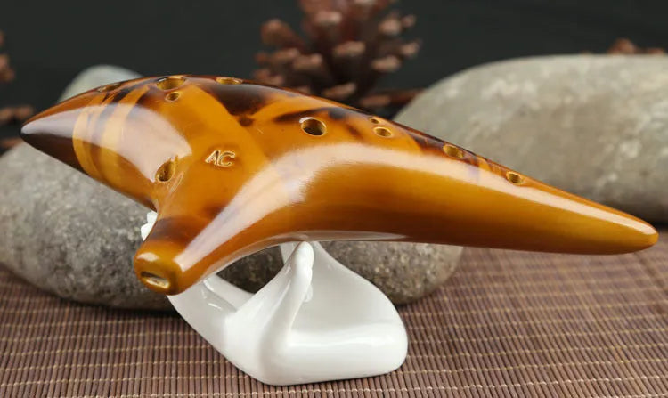 Yellow 12-hole ceramic Alto C ocarina with smoldering finish and lanyard on a surface