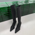 Black pointed-toe below-knee women's boots with a stiletto heel and a visible back zip on a neutral background.