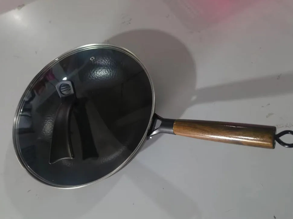 Traditional black iron wok with a long wooden handle on a kitchen counter.