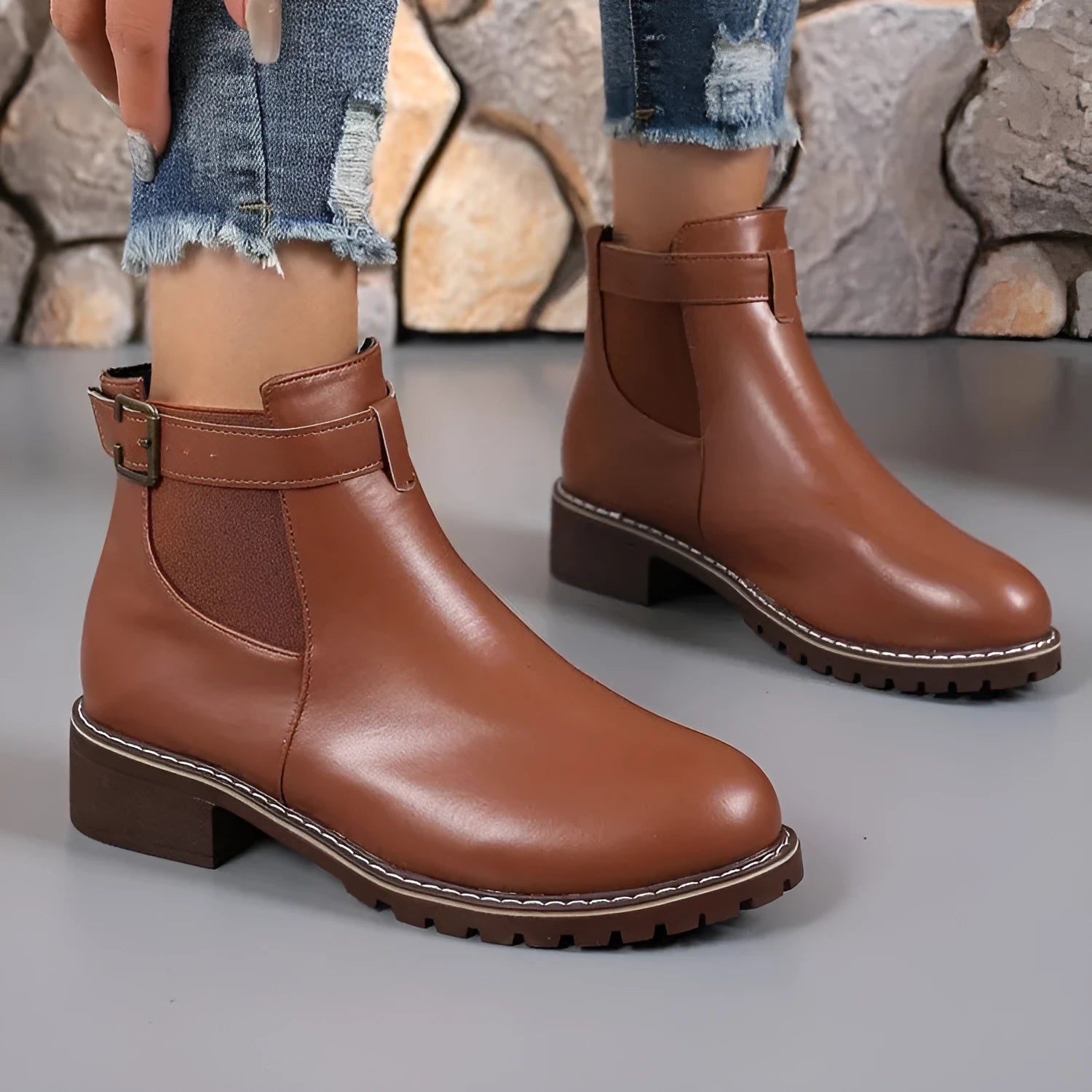 Black round toe women's ankle boot with a decorative metal belt buckle on the side.