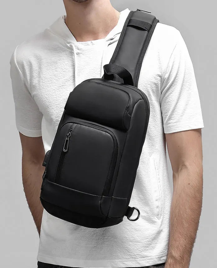 Black square PVC outdoor shoulder bag with an air cushion strap and zipper opening.