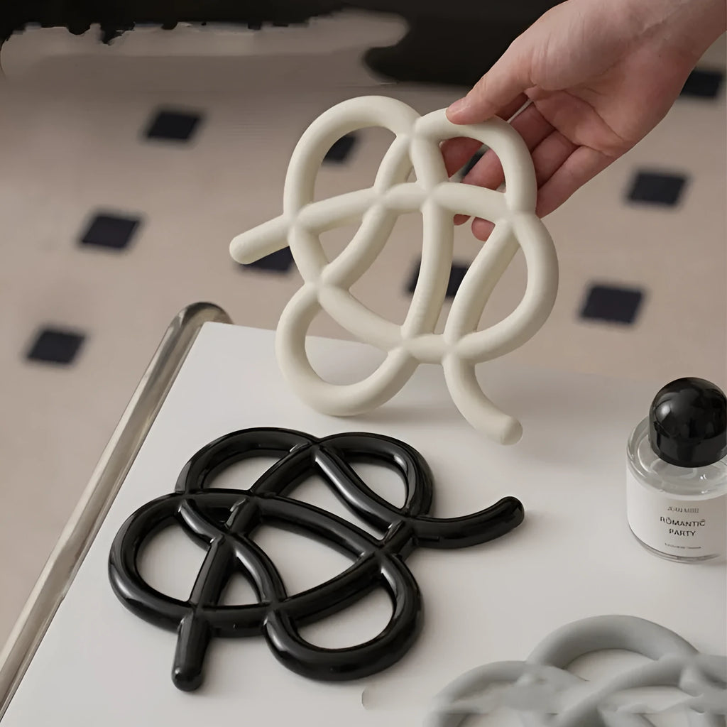 Irregular-shaped ceramic heat proof mat in grey on a wooden table next to a hot pan.