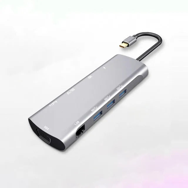 Grey aluminium USB-C docking station with HDMI, VGA, USB, and charging ports on a wooden desk.