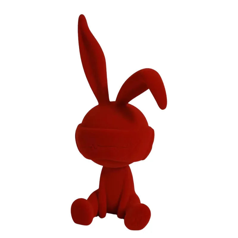 Suede blindfold rabbit resin ornament in blue, green, or red colour on a table.