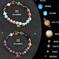 Twelve natural stone beaded bracelets with black cords and engraved crystal zodiac charms, laid out in a circle.