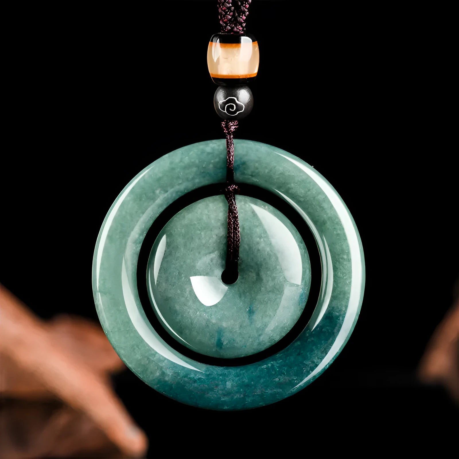 Emerald green jade pendant with carved national style design on a necklace stand
