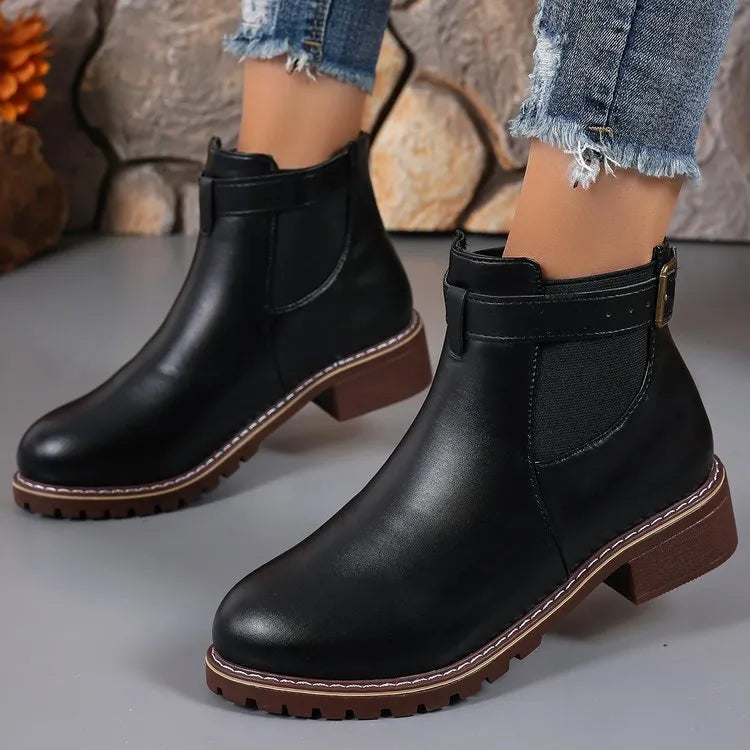 Black round toe women's ankle boot with a decorative metal belt buckle on the side.