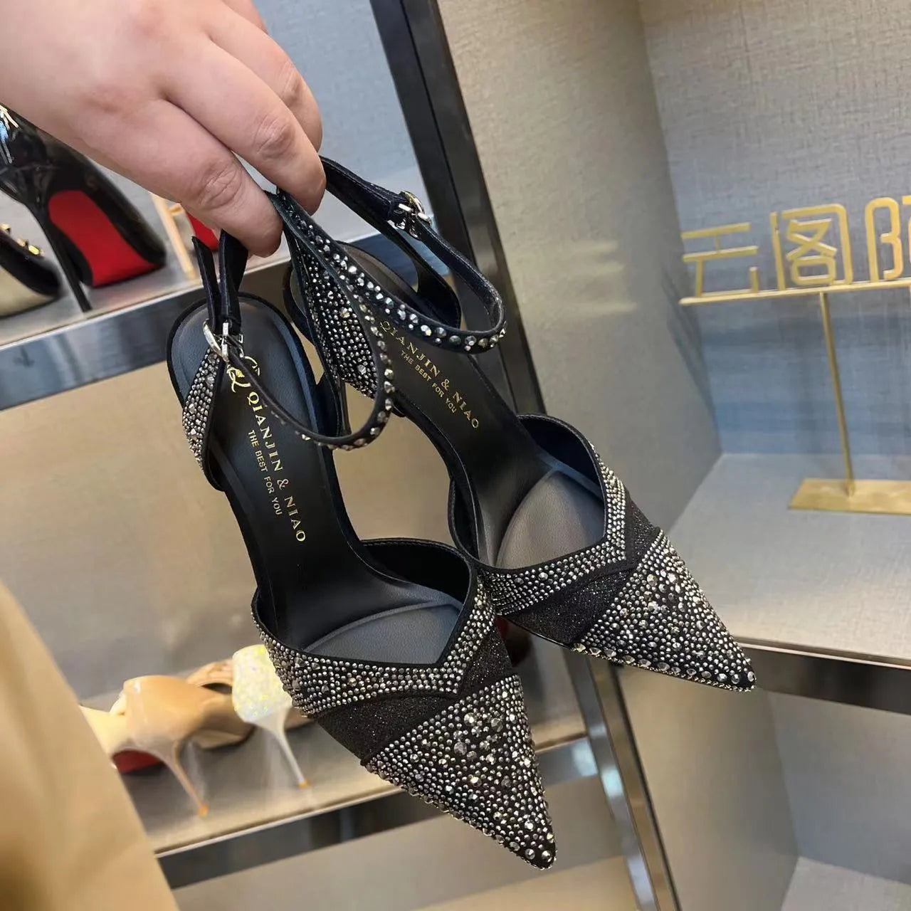 Women's black stiletto high heel with pointed toe and red sole, shown from the side.