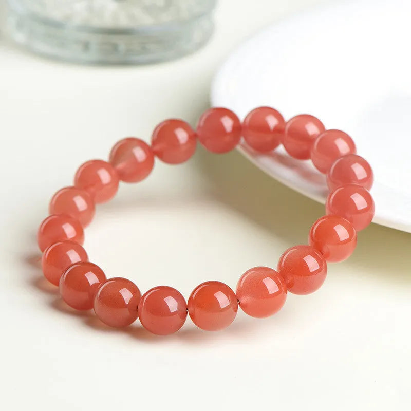 Natural cherry red agate beaded bracelet with adjustable metal clasp on a wrist, showing scattered polished stones.