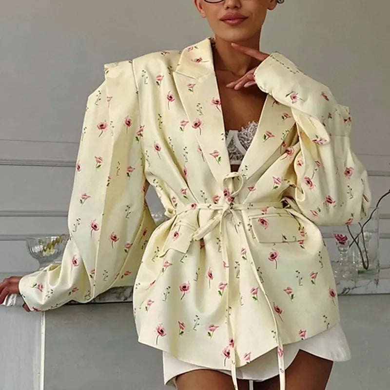 White floral print suit jacket with a lace-up detail at the waist on a hanger.