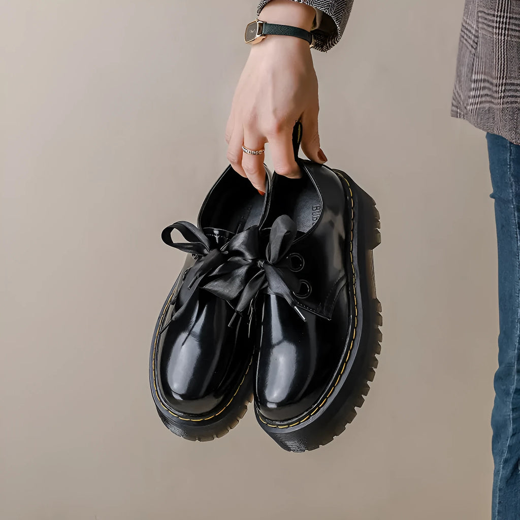White and black women's thick soled shoes with ribbon and cross straps and laced closure.