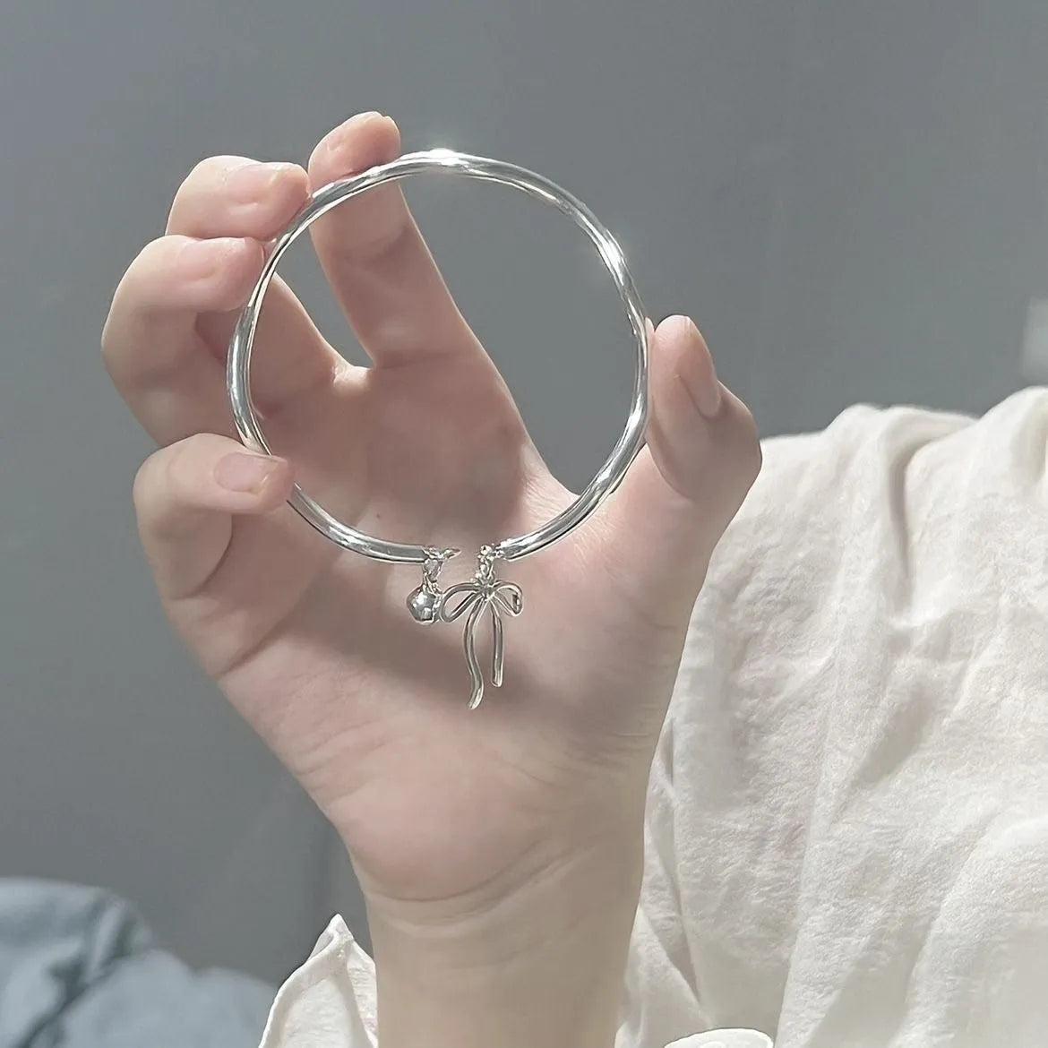 Silver tone adjustable bracelet with a 3D bow charm and magnetic clasp on a wrist.