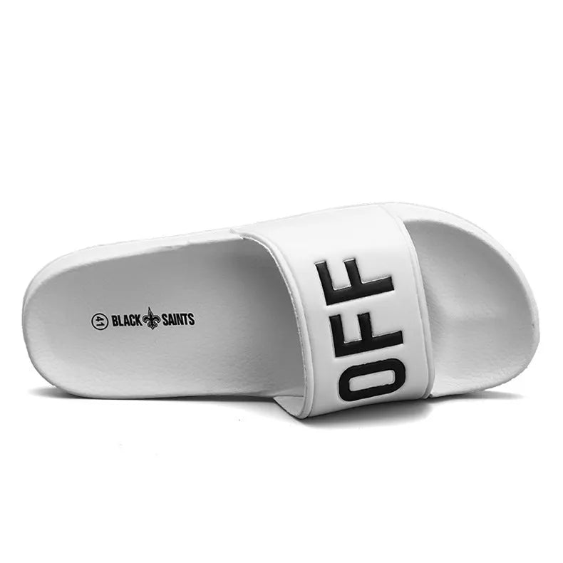 A pair of black open-toe men's slippers with a visible rubber sole, shown on a wooden floor.