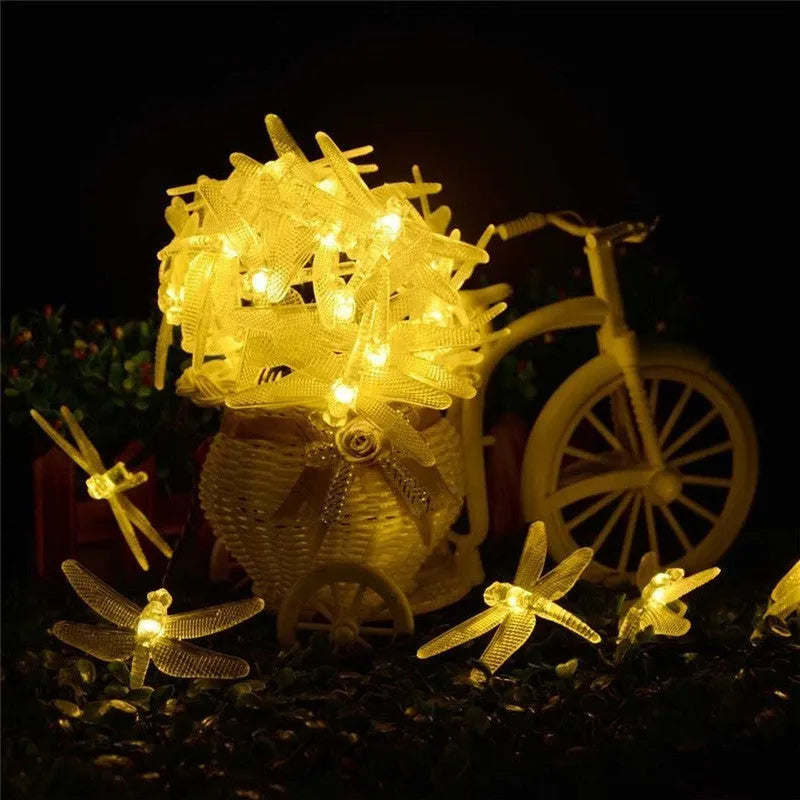 Solar powered outdoor LED string lights with dragonfly design showing warm white illumination in garden setting