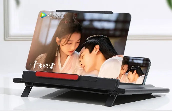 Black 12-inch mobile phone screen amplifier with pull-out stand on a table next to a phone.