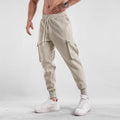 Man wearing loose-fit light grey cotton trousers with ankle ties and multiple pockets, suited for casual sports.