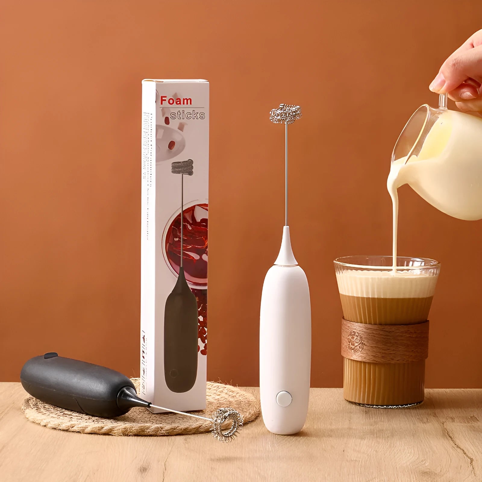 Handheld electric milk frother blender in black and white colour options on a kitchen counter.